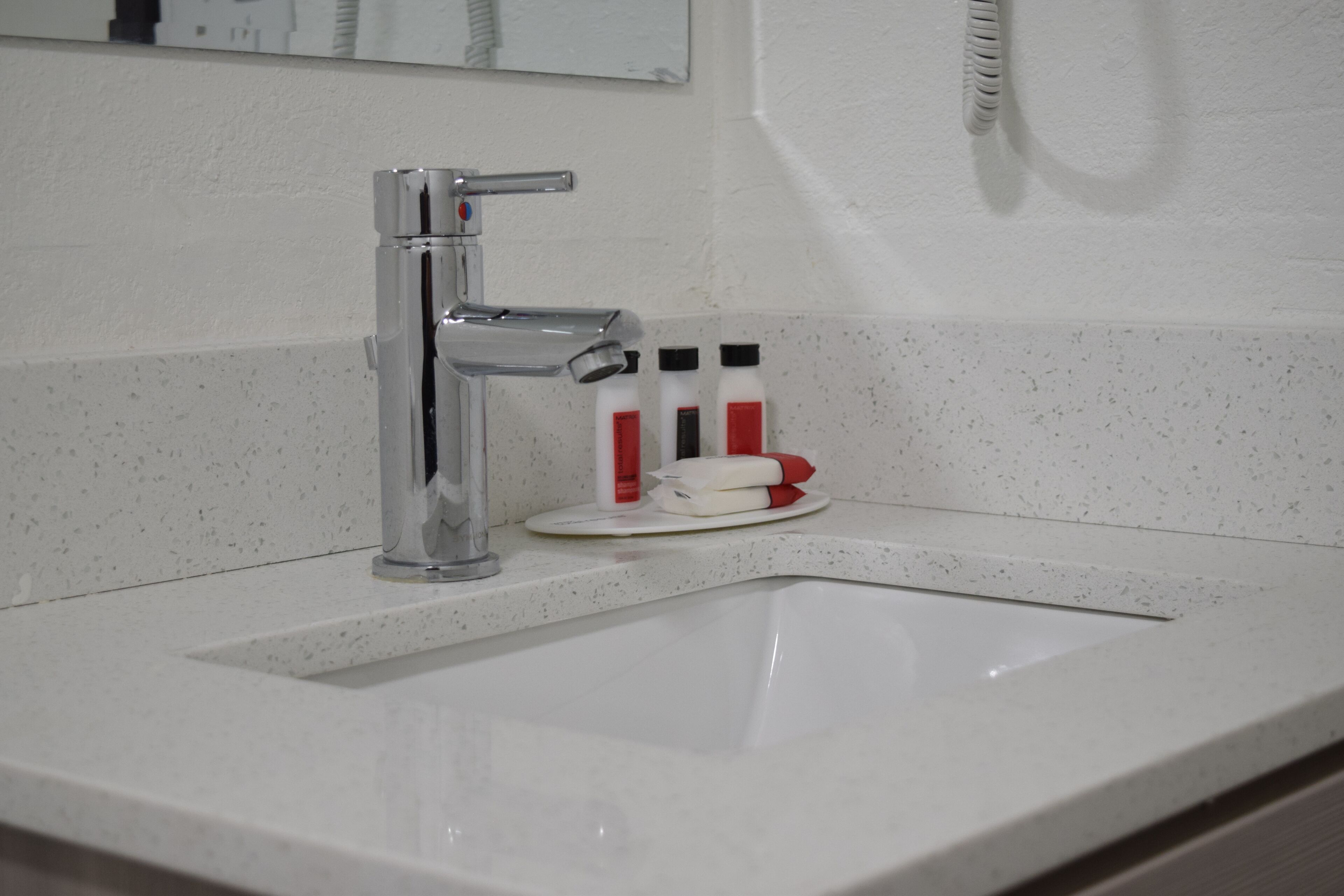 Ein Badezimmerwaschbecken mit chromfarbenem Wasserhahn, einer Seifenspender und einem Zahnbürstenhalter.