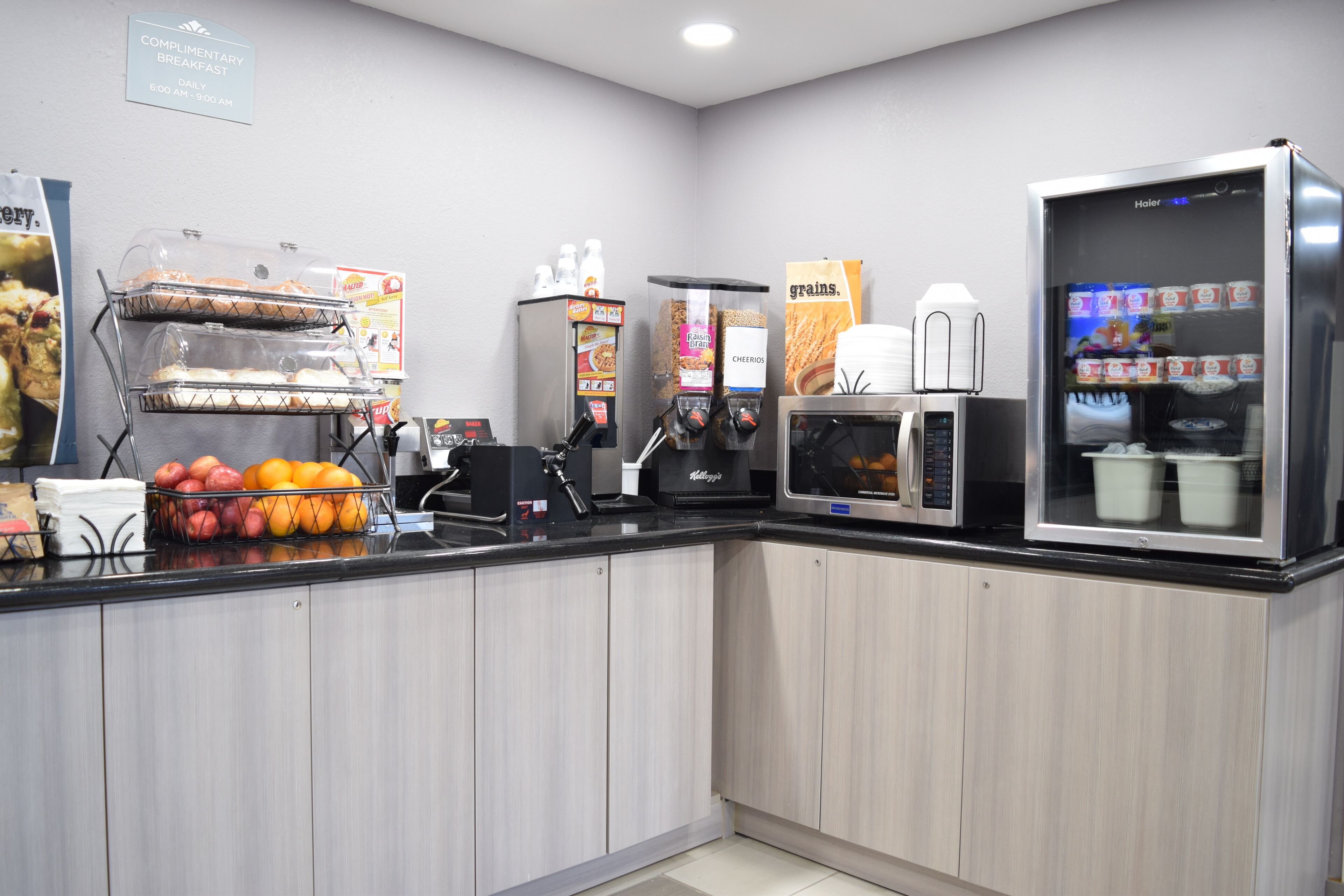 A breakfast area with a coffee machine, a microwave, a cereal dispenser, and a fruit display.