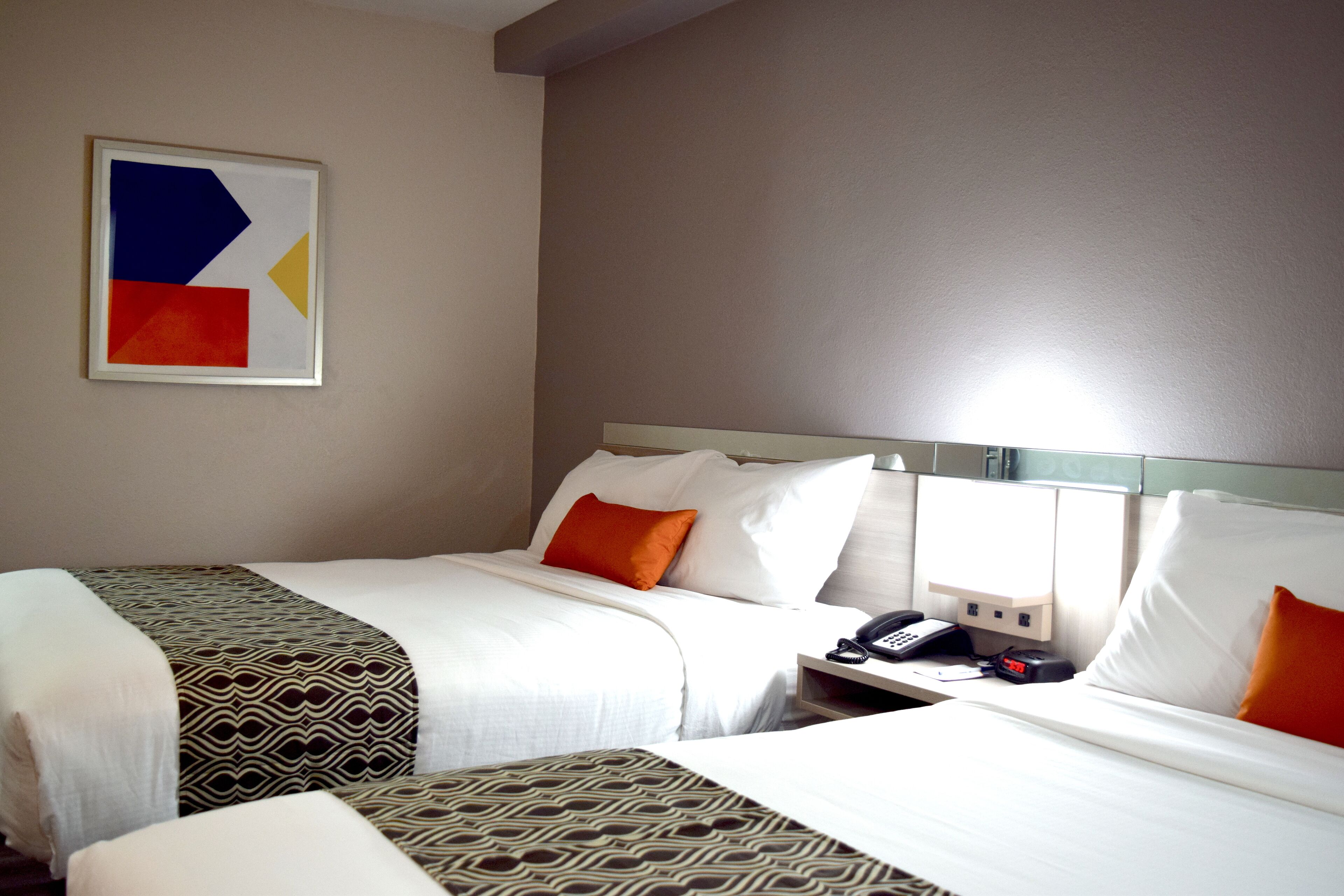 A hotel room with two beds, a nightstand with a phone, and a painting on the wall.