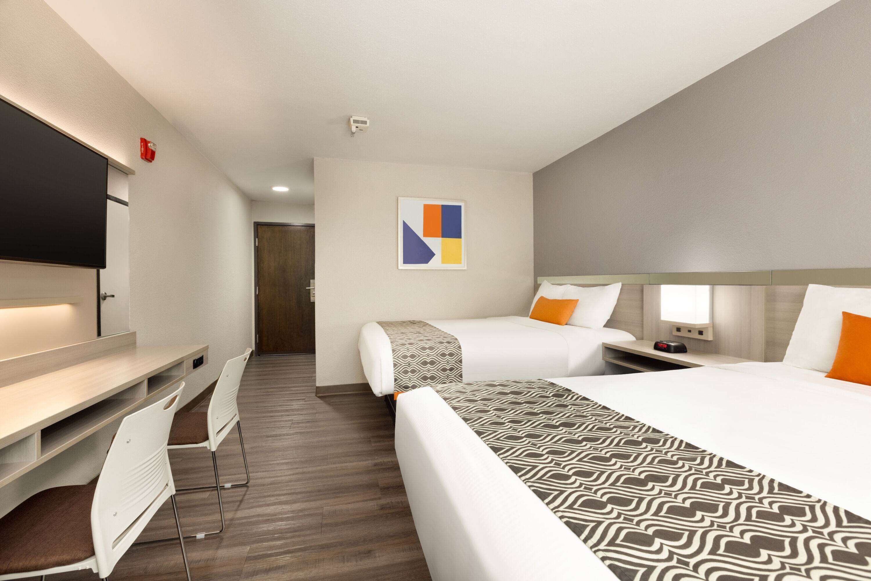 Ein Hotelzimmer mit Bett, Schreibtisch und Stuhl. An der Wand hängt ein Bild und es gibt ein Fenster.