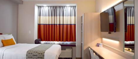 Habitación de hotel con dos camas, un escritorio, un espejo y una ventana con cortinas.
