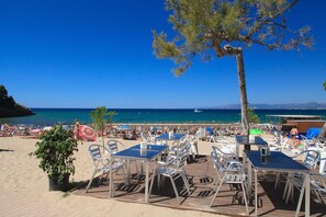 Un café situé en bord de mer, avec une terrasse, une vue sur l’océan et un ciel dégagé.