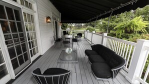 Un porche couvert avec une balustrade blanche, une table avec des chaises et un canapé noir.