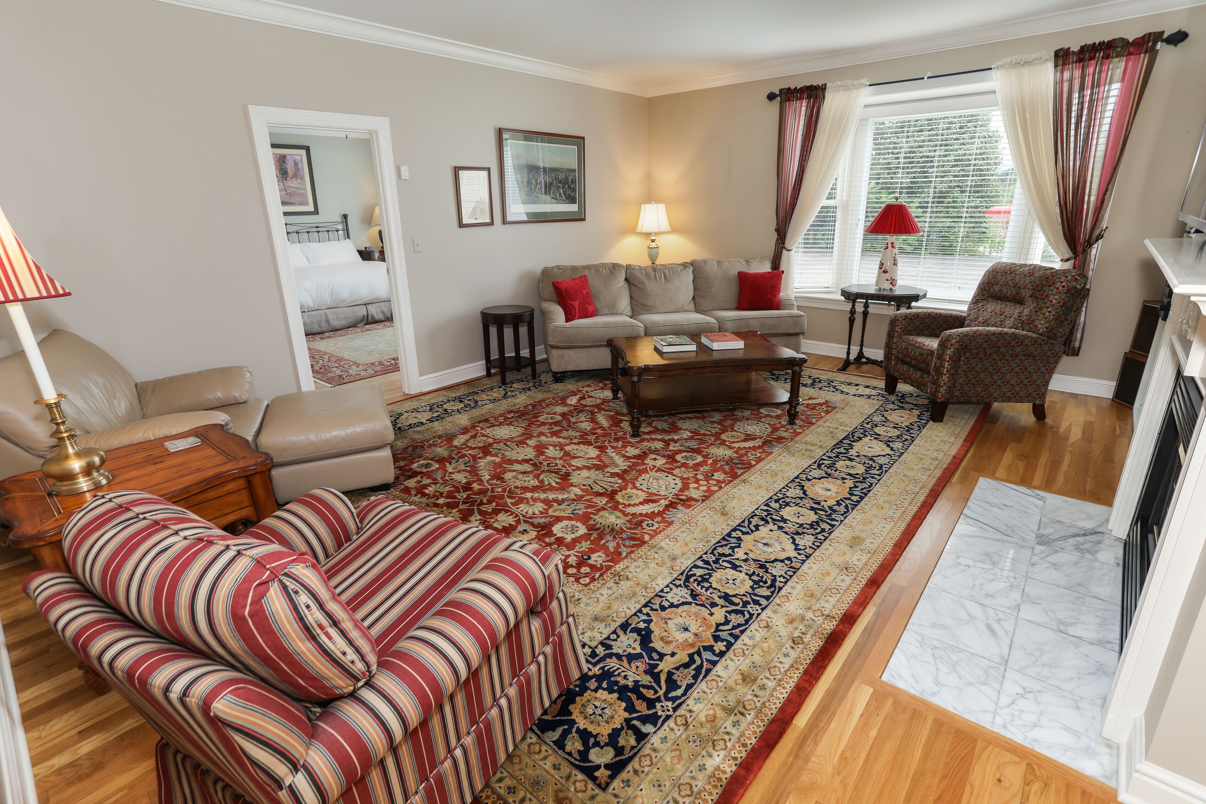 Un salon avec un canapé, un fauteuil et une table basse. Il y a une fenêtre avec des rideaux, une lampe et un tapis.