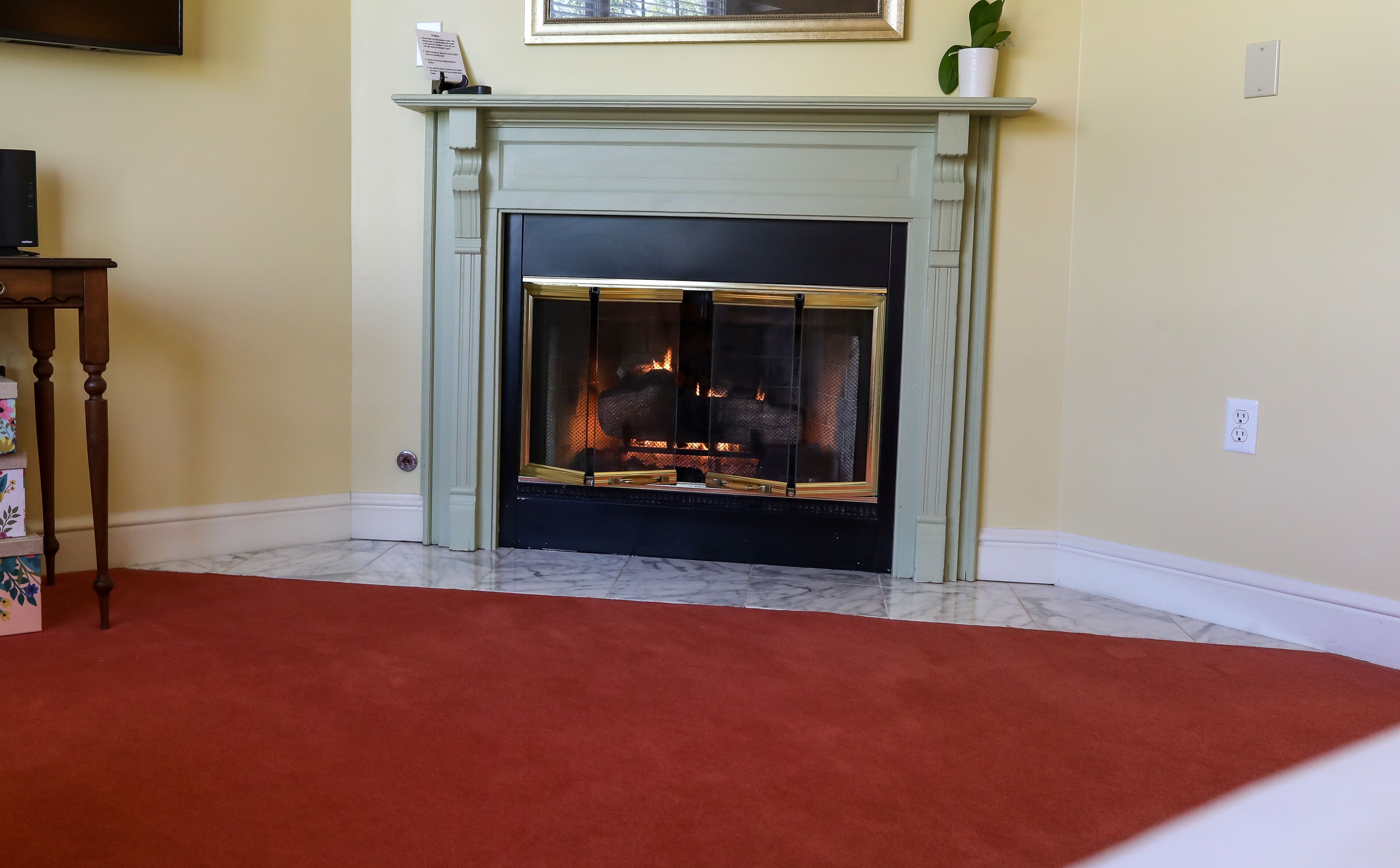 A fireplace with a fire, a television on a stand, and a red carpet.