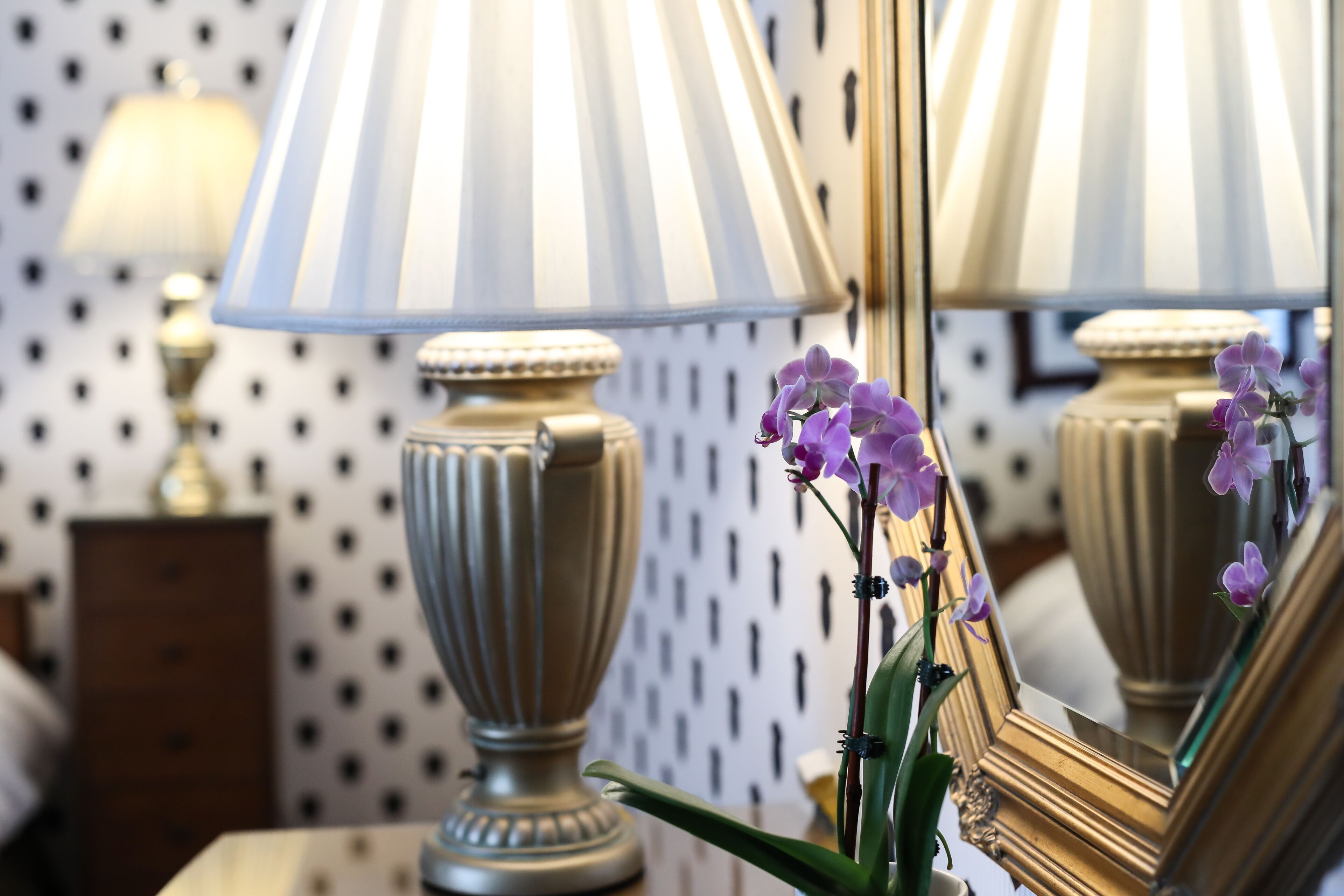 Une lampe dotée d’une surface réfléchissante et un vase orné de fleurs violettes.