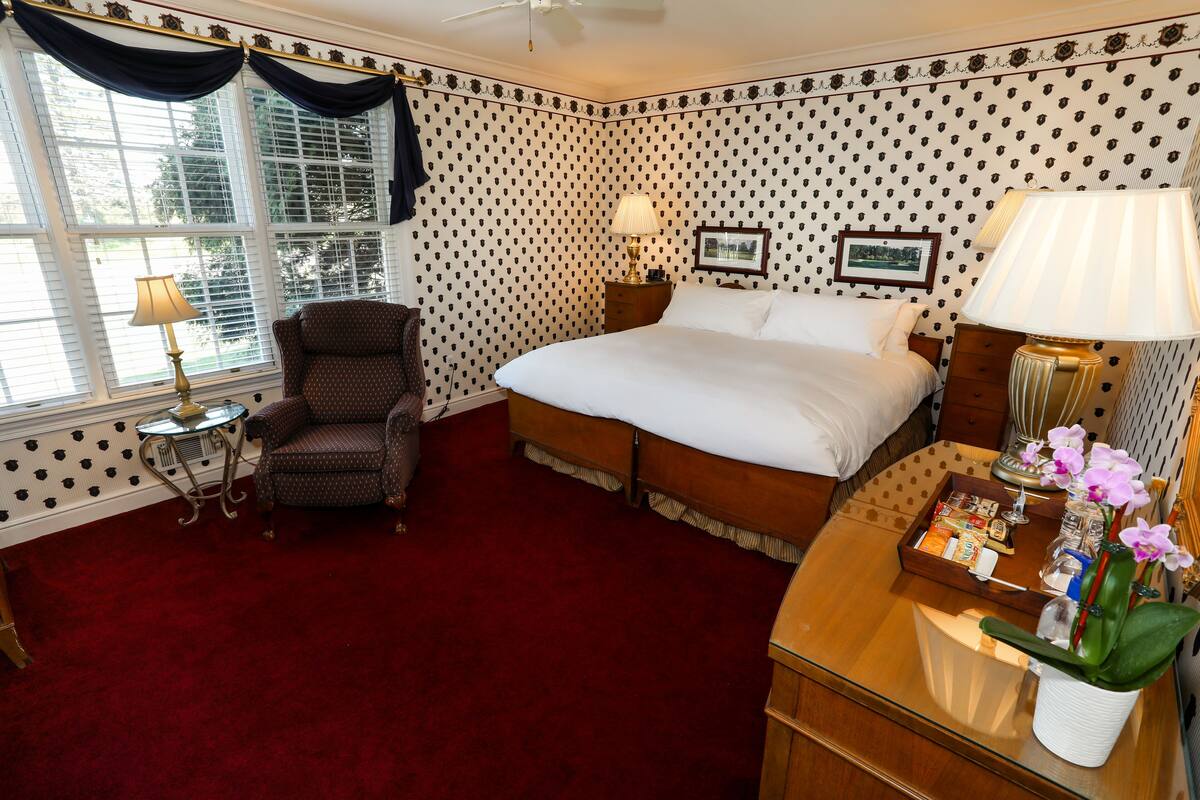 Ein Hotelzimmer mit einem großen Bett, einem Sessel, einem kleinen Tisch mit Lampe und einem Nachttisch ebenfalls mit Lampe.