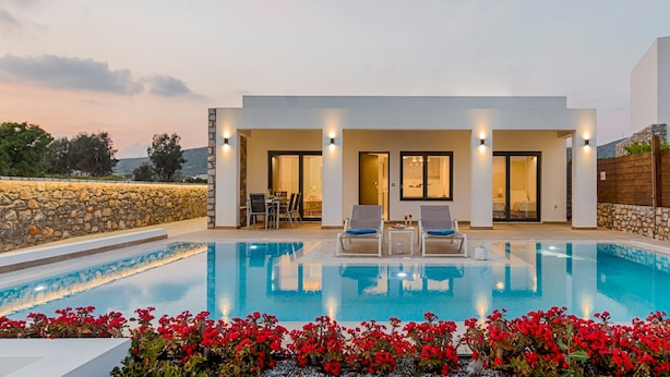 A modern poolside area with a clear pool, two lounge chairs, and a stone wall. - Prasonisi Villas (Rhodes)