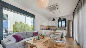 A modern living room with a sofa, coffee table, and a view of the kitchen. - Prasonisi Villas (Rhodes)
