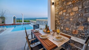 A dining area with a pool view, stone wall, and outdoor seating. - Prasonisi Villas (Rhodes)