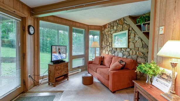 Un salon chaleureux avec un mur d’accent en pierre, un meuble de rangement en bois pour les appareils électroniques et un canapé confortable.