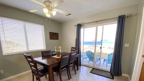 A dining area with a table and chairs, a ceiling fan, and a view of the beach through a glass door.