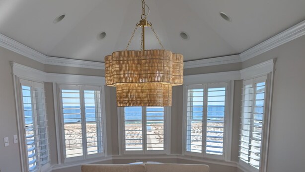 A dining room with a round table and chairs, large windows with a view of the beach, and a hanging chandelier. - Beautiful 5-bedroom 5-bathroom home on the Beach at the Jersey Shore (Point Pleasant Beach)