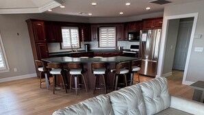 A modern kitchen with dark wood cabinets, a stainless steel refrigerator, and a central island with bar stools. - Beautiful 5-bedroom 5-bathroom home on the Beach at the Jersey Shore (Point Pleasant Beach)