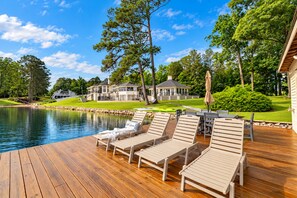 Eine Holzterrasse mit Liegestühlen und einem Pool, umgeben von Bäumen und einem großen Haus.