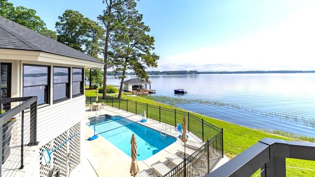 A pool area with a view of a lake, a gazebo, and a boat on the water.