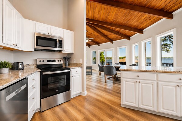 A modern kitchen with white cabinetry, stainless steel appliances, and a wooden ceiling.