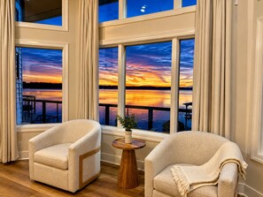 Una habitación con dos sillones, una pequeña mesa de madera y vistas a un atardecer sobre el agua.