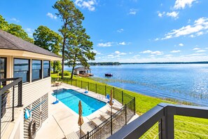 A swimming pool with a view of a lake, a covered seating area, and a fenced deck.