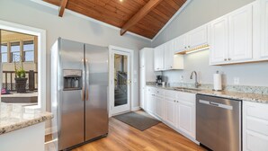 A modern kitchen with white cabinets, stainless steel appliances, and a wooden ceiling.