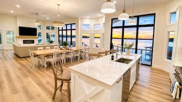 Une cuisine moderne dotée d’un grand îlot central, de planchers en bois et de grandes fenêtres offrant une vue sur l’extérieur.