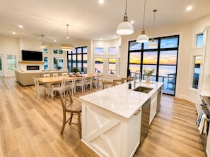 A modern kitchen with a large island, wooden flooring, and large windows offering a view of the outdoors.