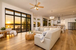 Amplia sala de estar con un sofá grande, una mesa de centro de madera y vistas a un lago al atardecer.