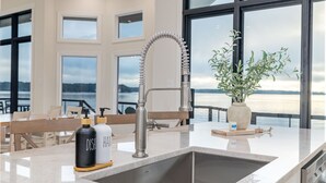 Une cuisine moderne dotée d’un évier en acier inoxydable, d’un robinet flexible et offrant une vue sur le lac grâce à de grandes fenêtres.