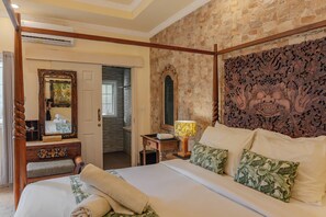 A hotel room with a large bed, a wooden headboard, a mirror, a nightstand, and a bathroom visible through an open door. - Menzel Villa (Nusa Dua)