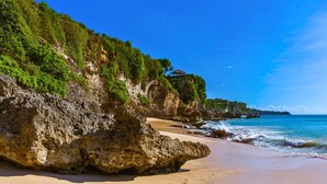 A beach with a rocky cliff and a building on top. - Menzel Villa (Nusa Dua)