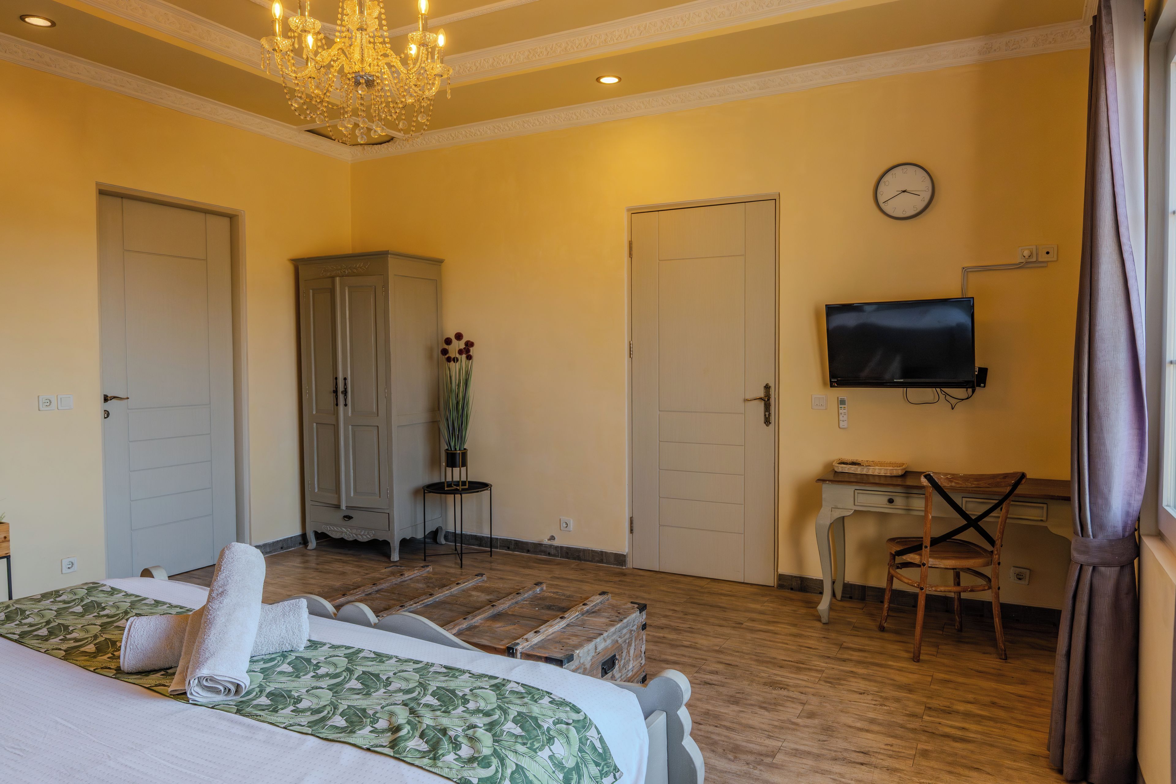 Una habitación de hotel con cama, escritorio, televisor, armario y candelabro.
