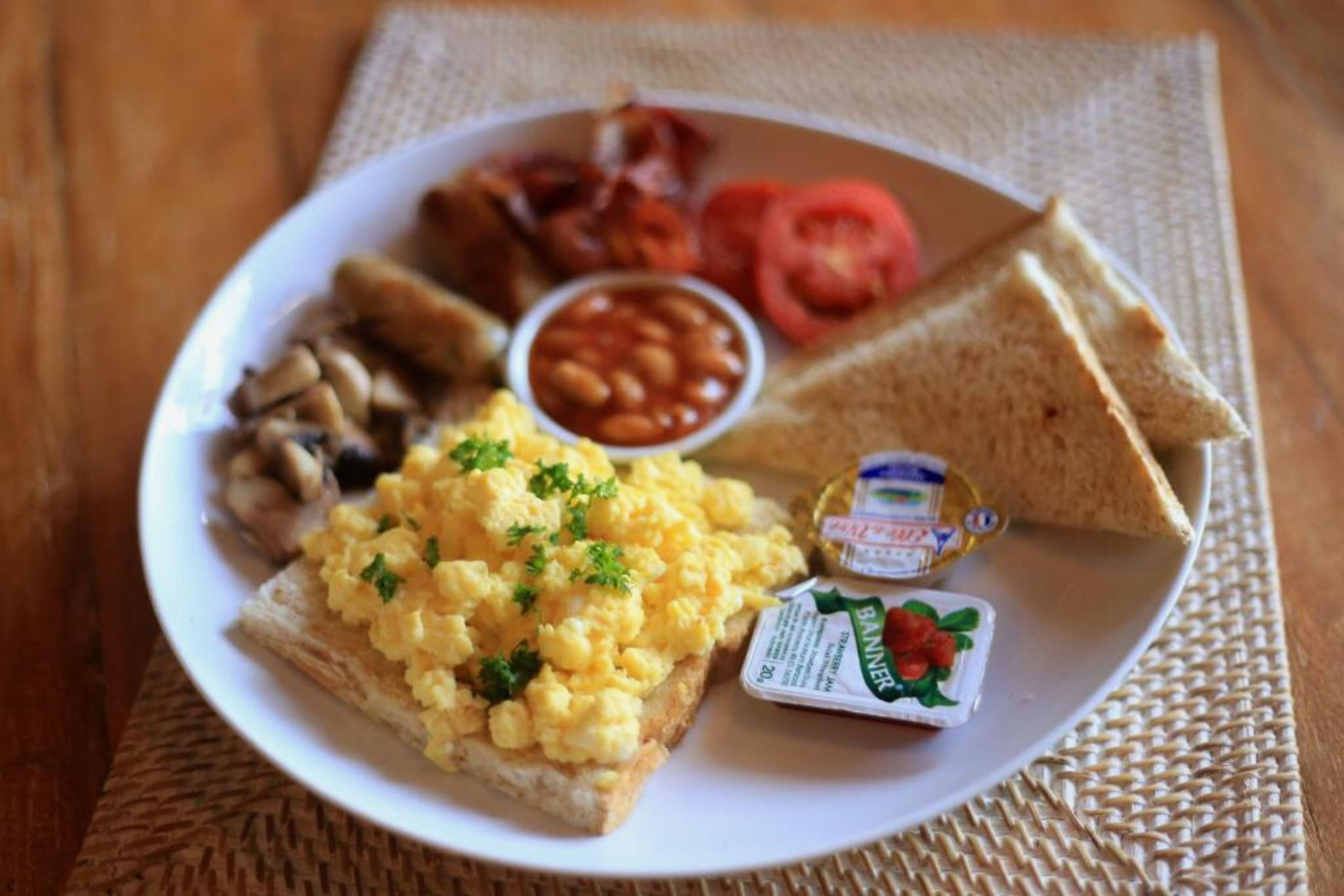 A plate of breakfast food including toast, scrambled eggs, beans, tomatoes, and bacon.
