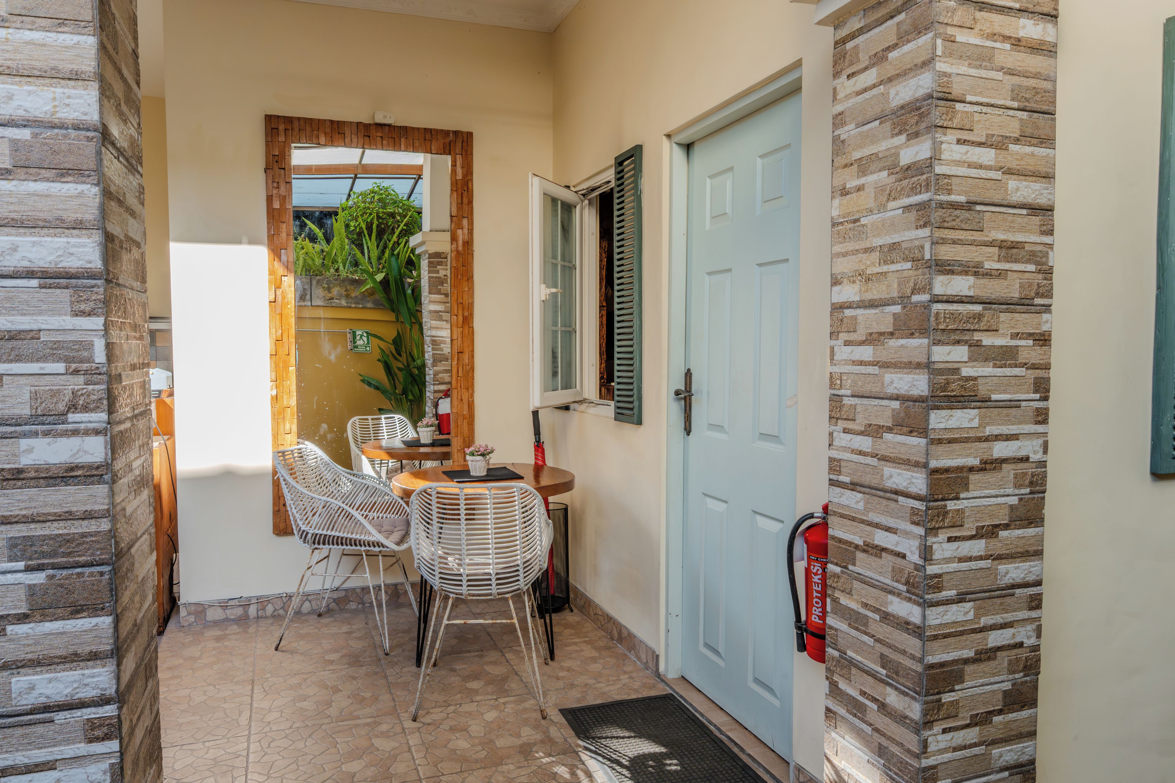 A small outdoor seating area with wicker chairs and a table, a blue door, and a fire extinguisher mounted on the wall.