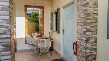 A small outdoor seating area with wicker chairs and a table, a blue door, and a fire extinguisher mounted on the wall.