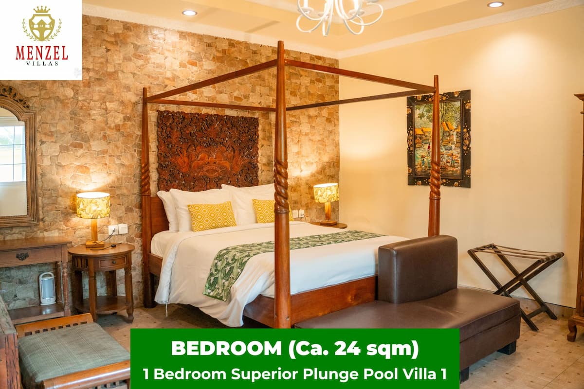 A bedroom with a stone wall, a four-poster bed, two bedside lamps, a nightstand, a bench, and a painting on the wall.