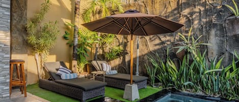 Un espace aménagé au bord de la piscine, avec une chaise longue, une petite table et un parasol.