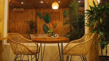 A room with a round wooden table, two wicker chairs, and a large potted plant.