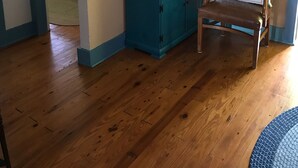A room with a wooden floor, a teal dresser with drawers, a clock, a framed picture, and a chair with a beach pillow. - Cottage On Famous Chincoteague Island-Famous Wild Ponies (Chincoteague Island)