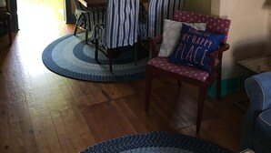 A dining area with striped chairs, a table, and a round rug. There is a painting on the wall, a window with curtains, and a starfish decoration. - Cottage On Famous Chincoteague Island-Famous Wild Ponies (Chincoteague Island)