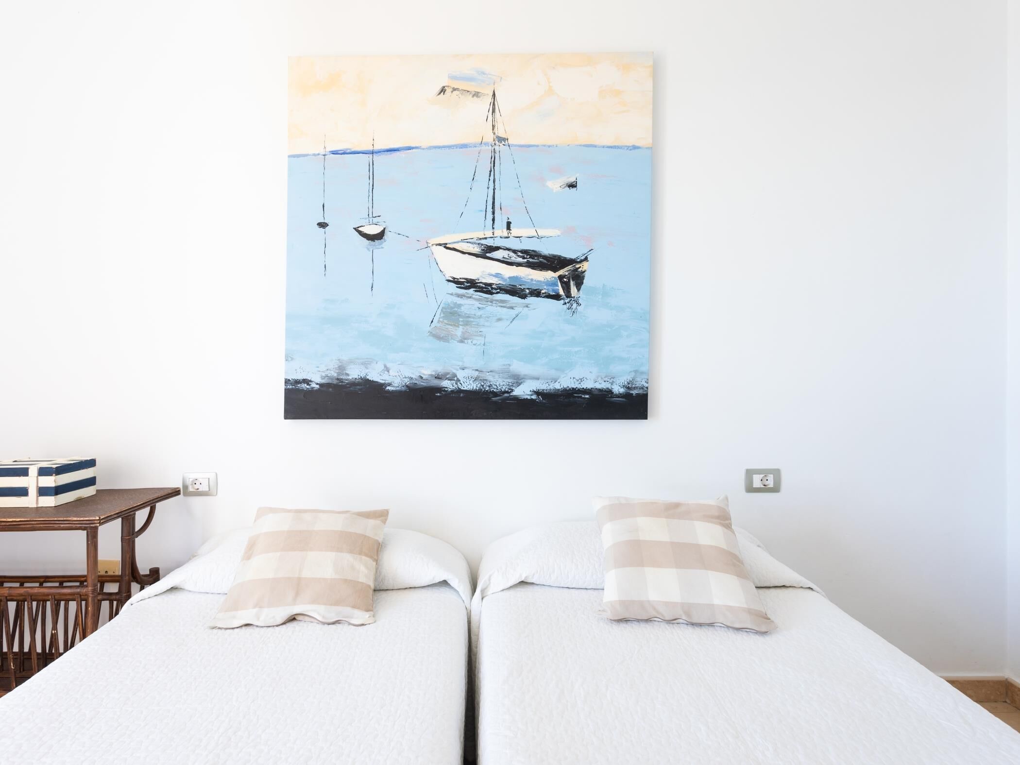 Une chambre avec deux lits, une table de chevet en bois et un tableau représentant des bateaux sur l’eau.