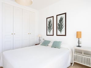 Una camera da letto con un letto grande, pareti bianche e due opere d'arte con foglie in cornice.