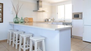 A modern kitchen with white cabinetry, a central island with bar stools, a stainless steel range hood, and a built-in microwave. - Beautiful sea view duplex - PORÍS 1 (Poris de Abona)