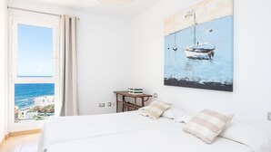 A bedroom with a bed, a view of the sea, a painting of boats, and a small table with a lamp. - Beautiful sea view duplex - PORÍS 1 (Poris de Abona)