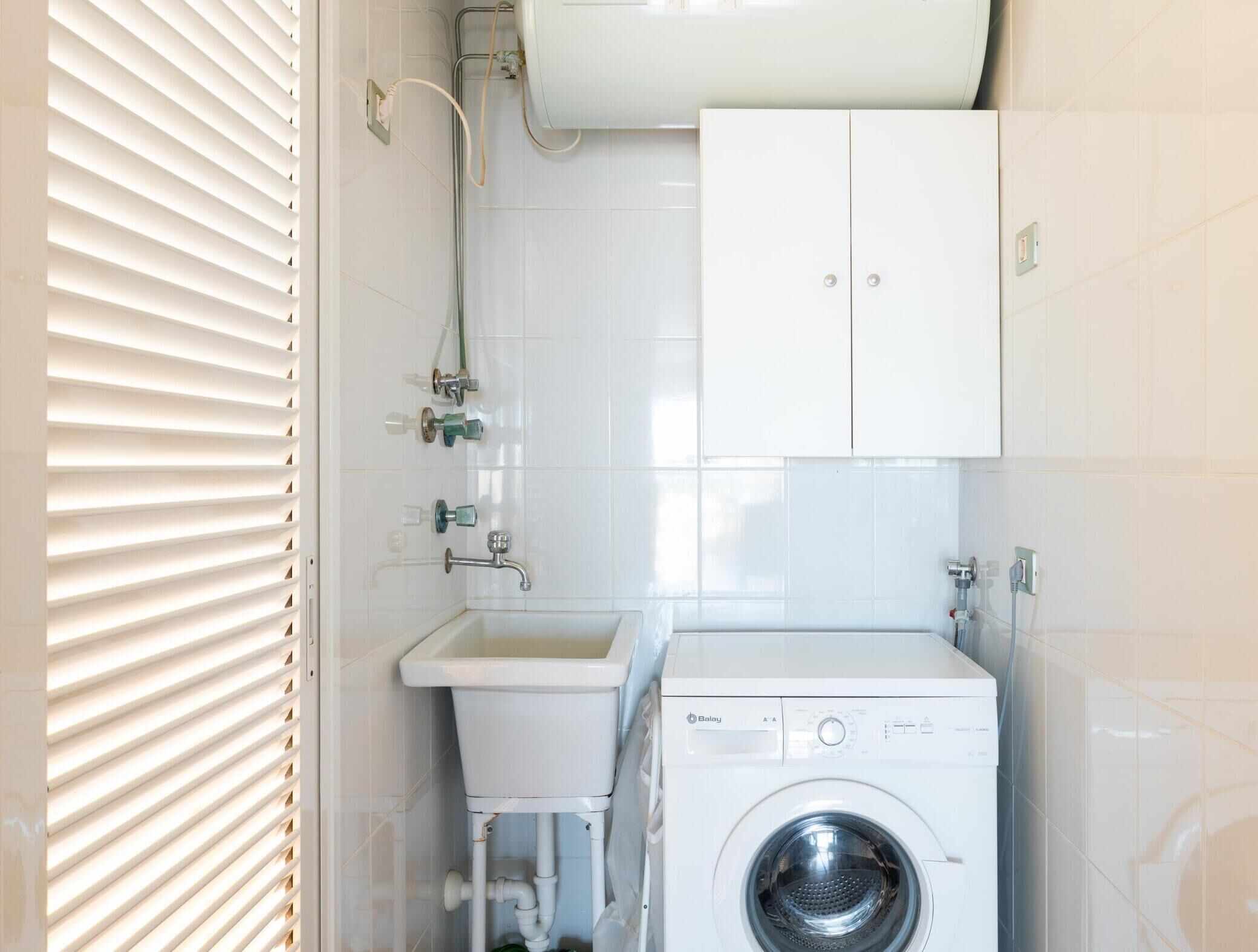 A small, clean laundry room with a washing machine, a sink, and a cabinet.