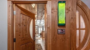 Une porte en bois donne sur une pièce dotée d’une grande fenêtre, d’un panneau décoratif vert et d’un tableau encadré accroché au mur.