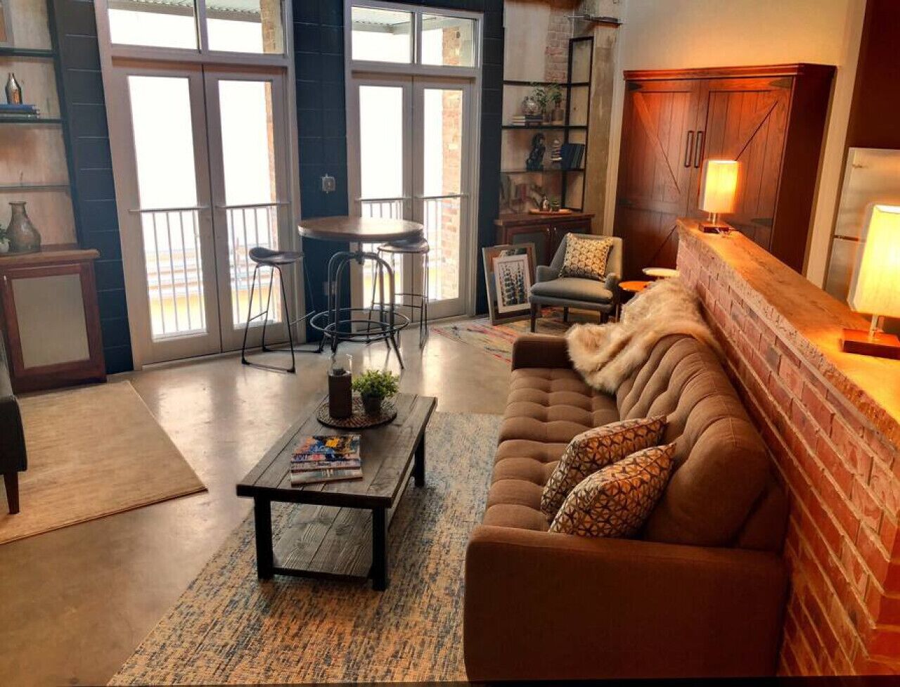 A cozy living room with a brown sofa, a coffee table, and a fireplace. There is a dining area with a table and chairs, and a kitchen area with cabinets and a refrigerator.