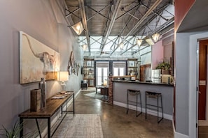 Exposed metal beams meet modern style in this stylish space, featuring a large abstract painting and a cozy dining area with a bar counter.