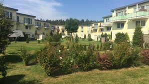 A residential complex with multiple two-story buildings, each featuring balconies and a garden area with various plants and flowers.