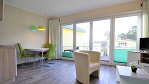A modern living room with a dining area, large windows, and a TV.