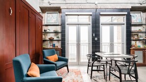 A room with a wooden wardrobe, two blue armchairs with orange cushions, a round table with chairs, and a patterned rug. - Green Door Lofts-Retro Loft - Silos/Downtown (Waco)